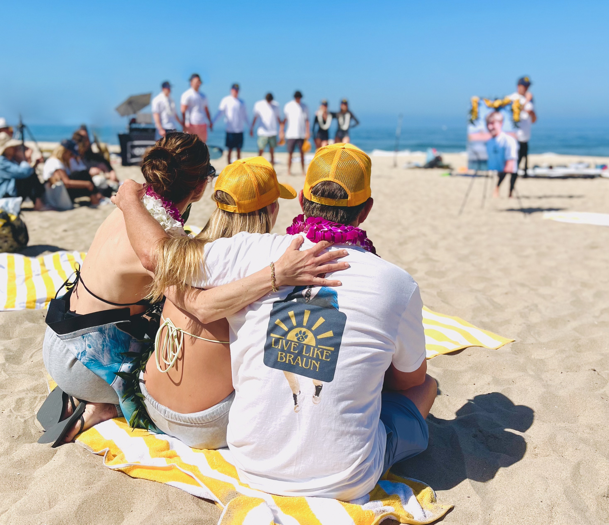 A picture of a mom, dad and daughter with their arms around each other on the beach at their son's paddle out memorial.