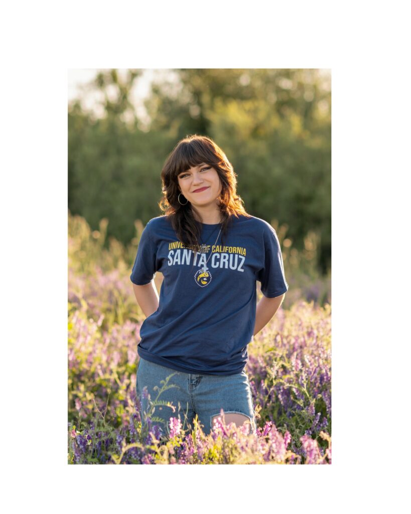 A senior in high school from Oak Ridge high school is posing in a field of wildflowers with her UCSC Santa Cruz college T-shirt on.